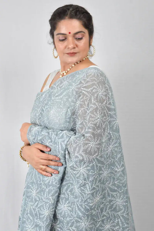 Woman wearing a light blue saree with white patterns on a plain background