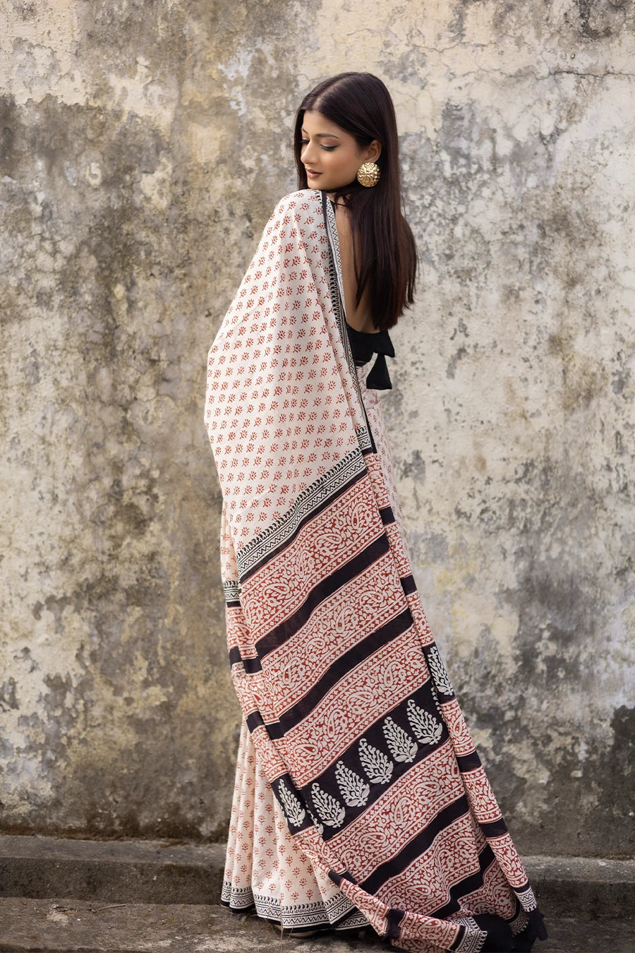 Woman wearing a patterned saree against a textured wall.