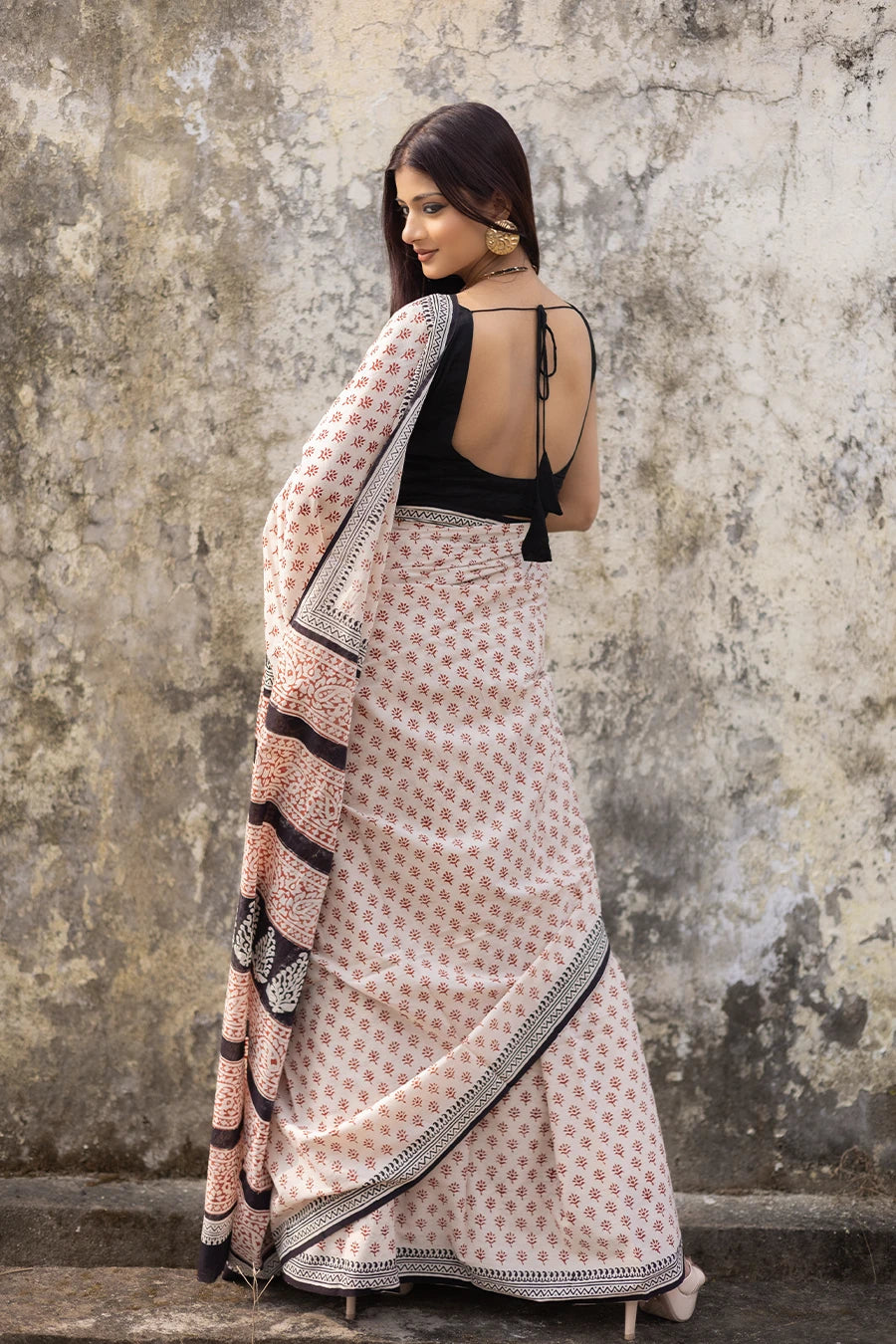 Woman wearing a patterned saree against a textured wall.
