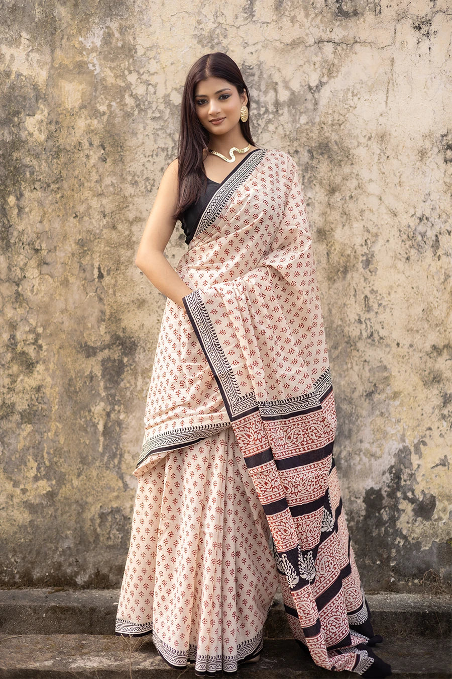 Woman wearing a patterned saree against a textured wall.