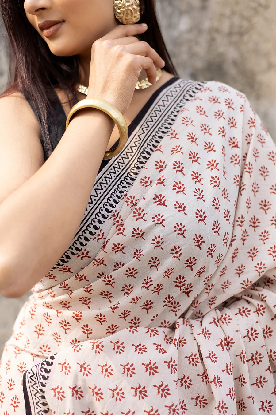 Woman wearing a patterned saree against a textured wall.