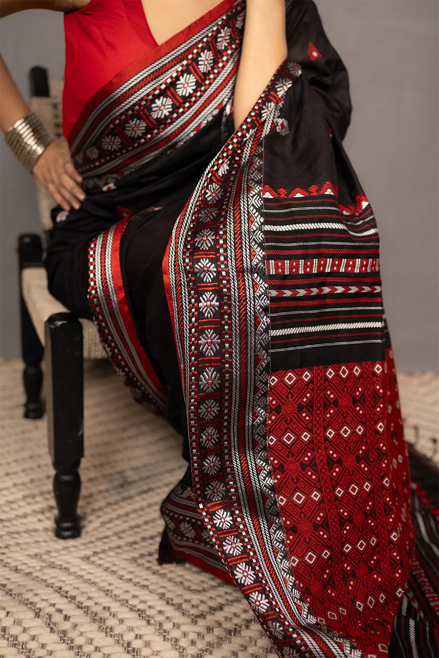 Woman wearing a black and red saree with a chair in the background