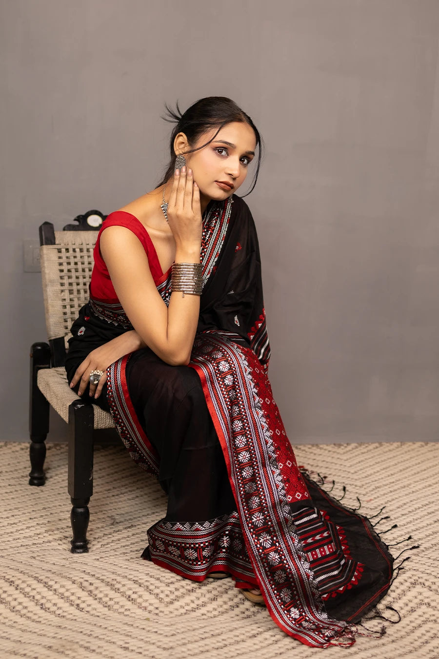 Woman wearing a black and red saree with a chair in the background