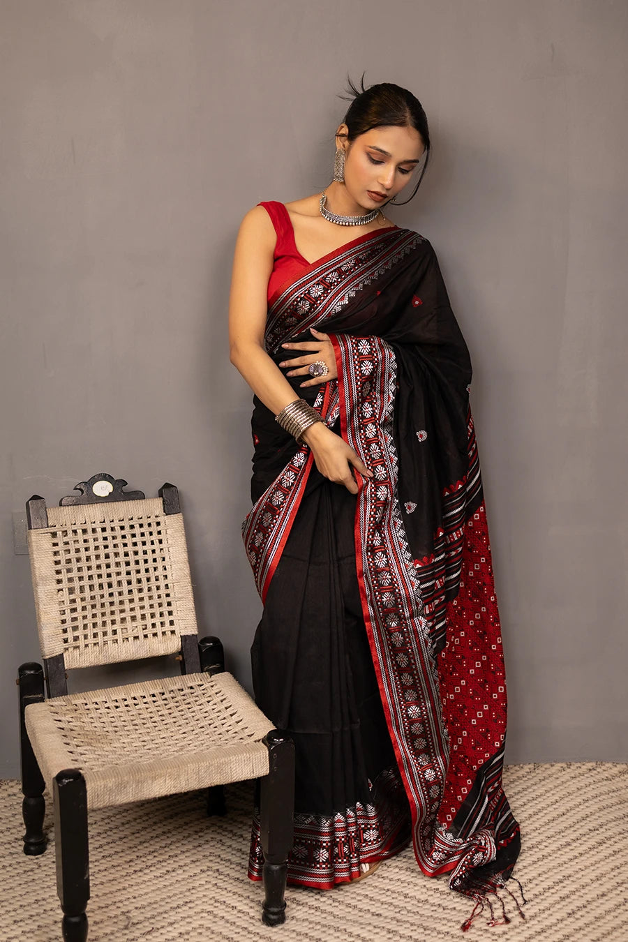 Woman wearing a black and red saree with a chair in the background