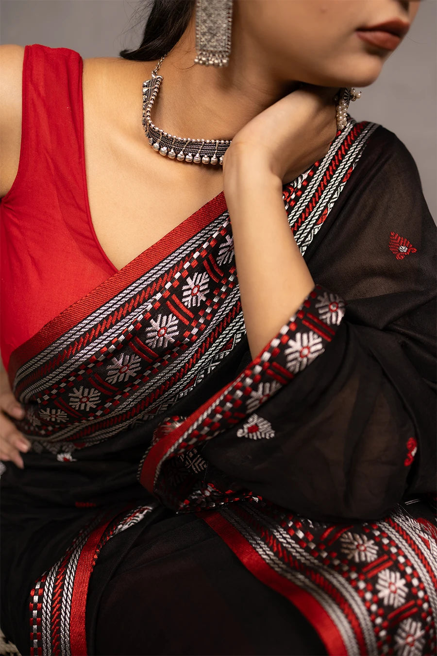 Woman wearing a black and red saree with a chair in the background