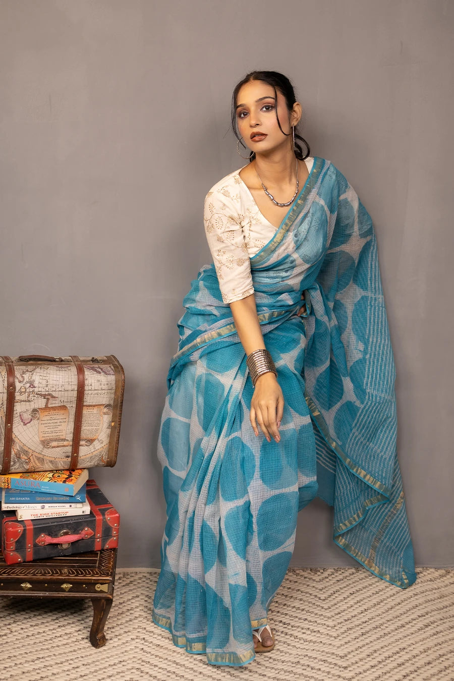 Woman in a blue saree with white patterns standing against a grey wall.