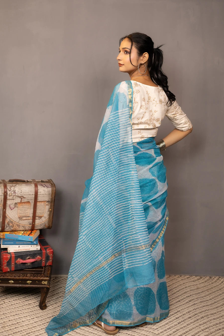 Woman in a blue saree with white patterns standing against a grey wall.