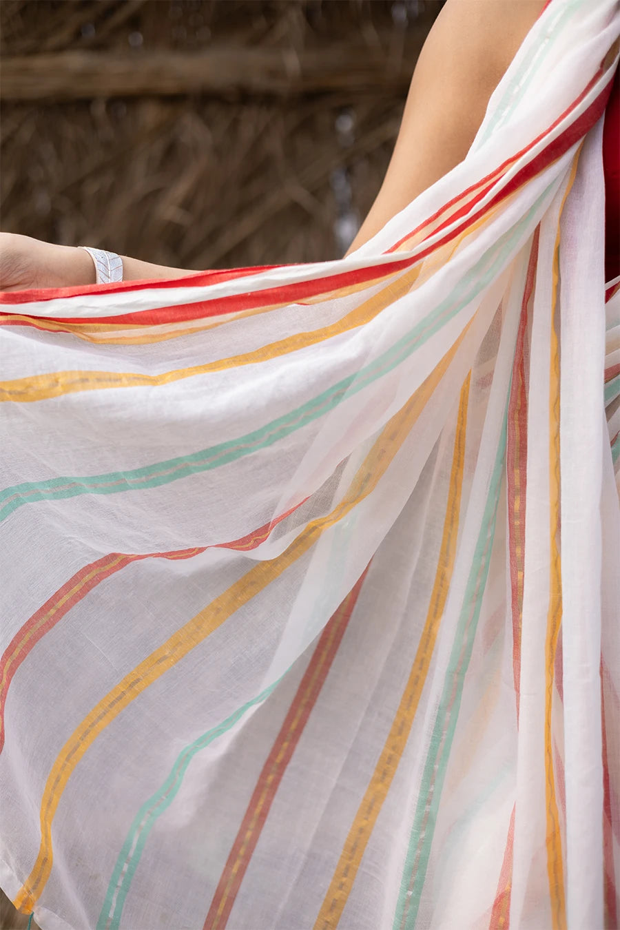 Woman in a colorful saree with tassels standing against a rustic background