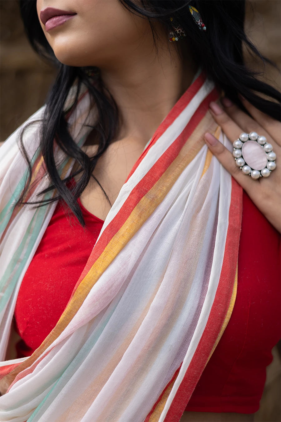 Woman in a colorful saree with tassels standing against a rustic background