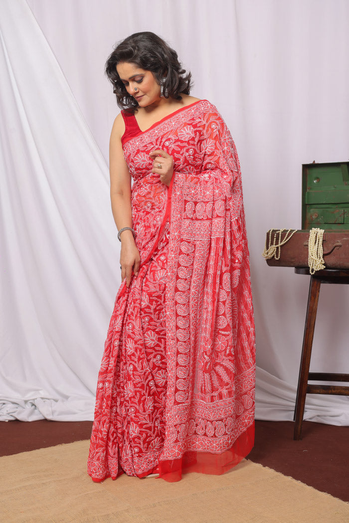 A woman showcasing a red color georgette saree with chikankari embroidery and a matching blouse piece.