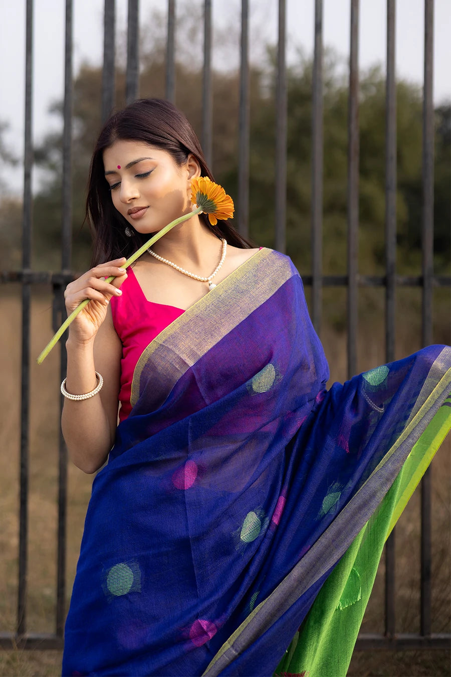 Woman wearing a blue and green saree with a pink blouse, standing outdoors.
