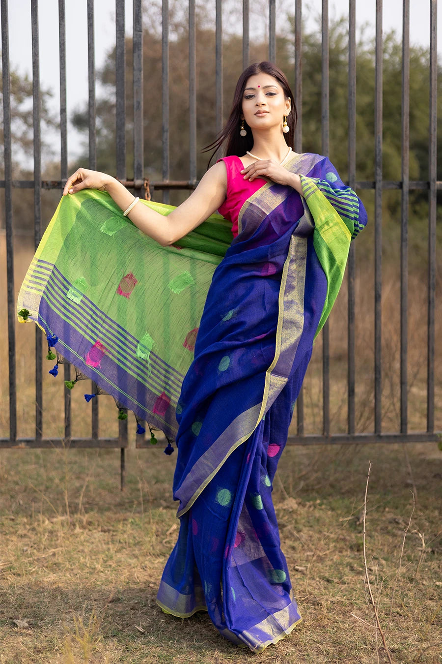 Woman wearing a blue and green saree with a pink blouse, standing outdoors.