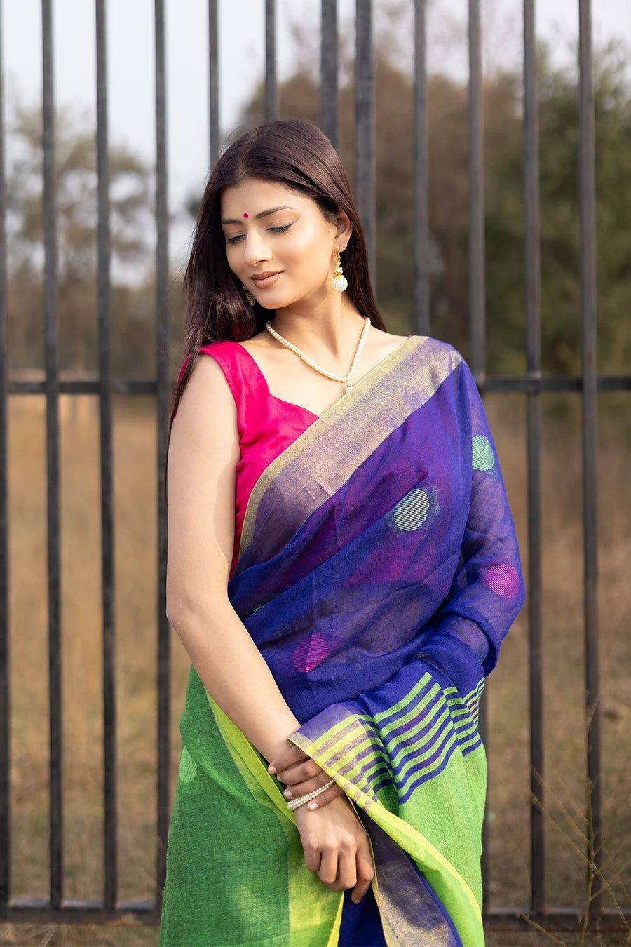 Woman wearing a blue and green saree with a pink blouse, standing outdoors.