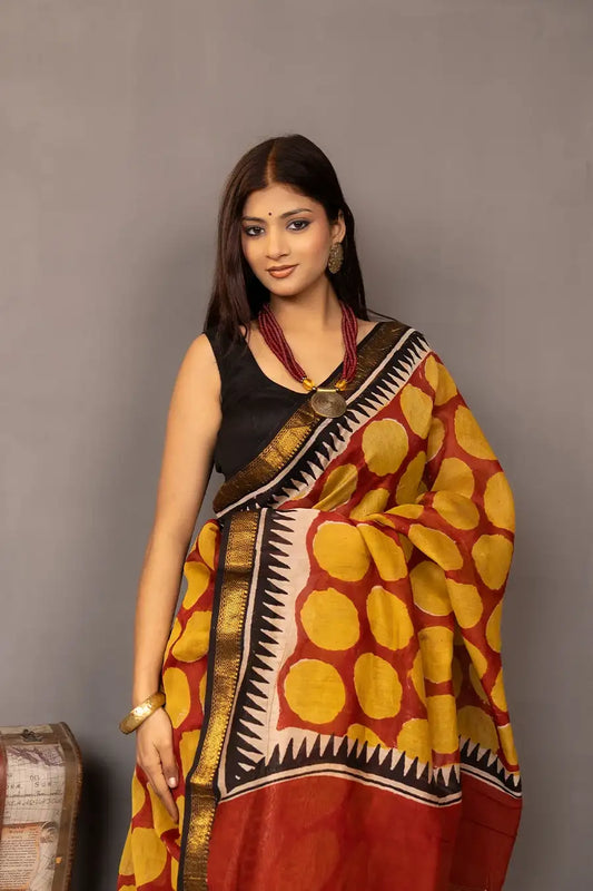 Woman wearing a traditional saree with a patterned design, standing next to a small table with books and a suitcase.
