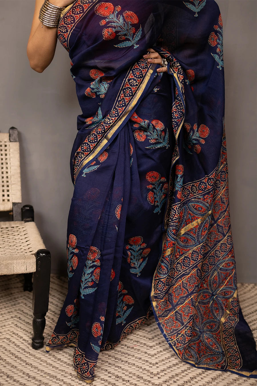 Woman wearing a blue saree with a red blouse against a grey background