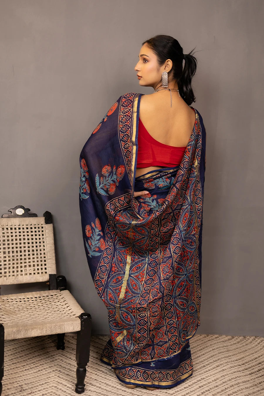 Woman wearing a blue saree with a red blouse against a grey background