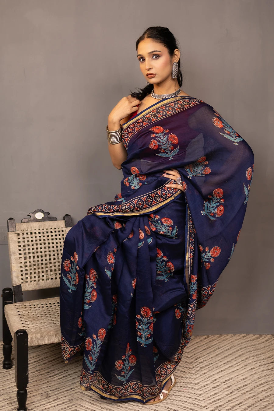 Woman wearing a blue saree with a red blouse against a grey background