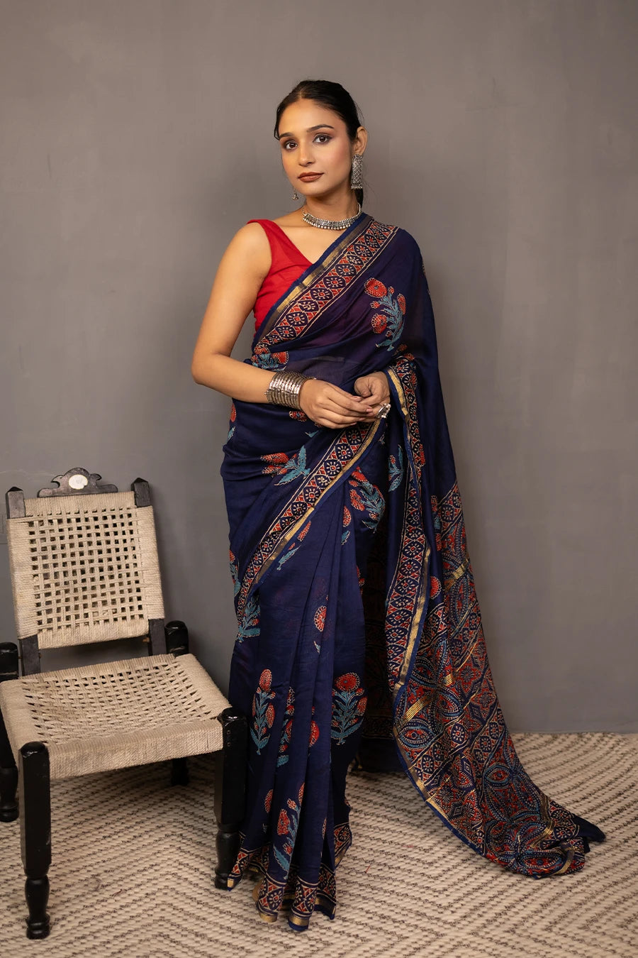 Woman wearing a blue saree with a red blouse against a grey background