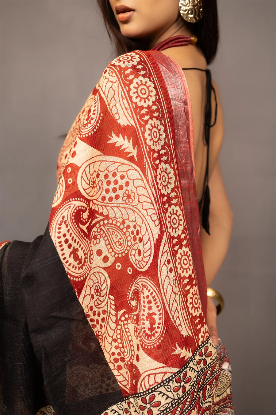 Woman wearing a traditional saree with a patterned design, standing next to a small table with books and a suitcase.