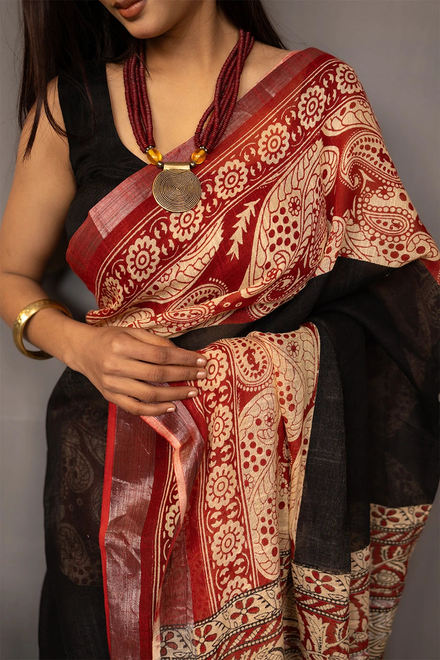 Woman wearing a traditional saree with a patterned design, standing next to a small table with books and a suitcase.