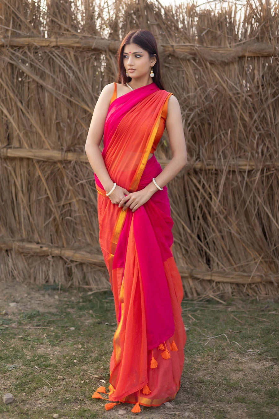 Model wearing a magenta and orange mul cotton saree with contrast border and tassel detailing, suitable for daily wear, casual outings, and festive occasions.