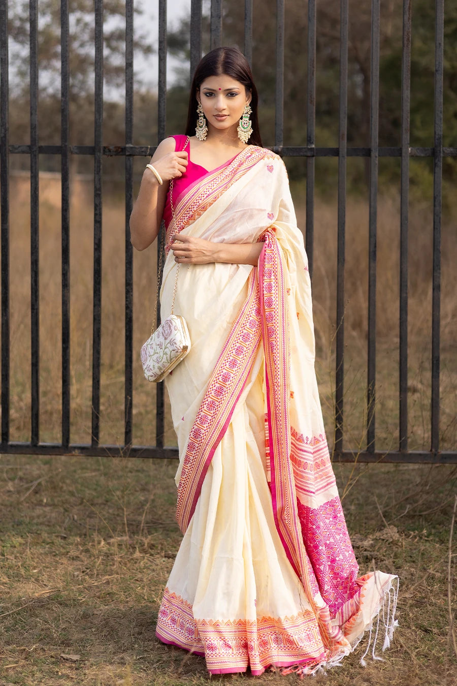 Woman wearing a white and pink saree with a black metal gate in the background