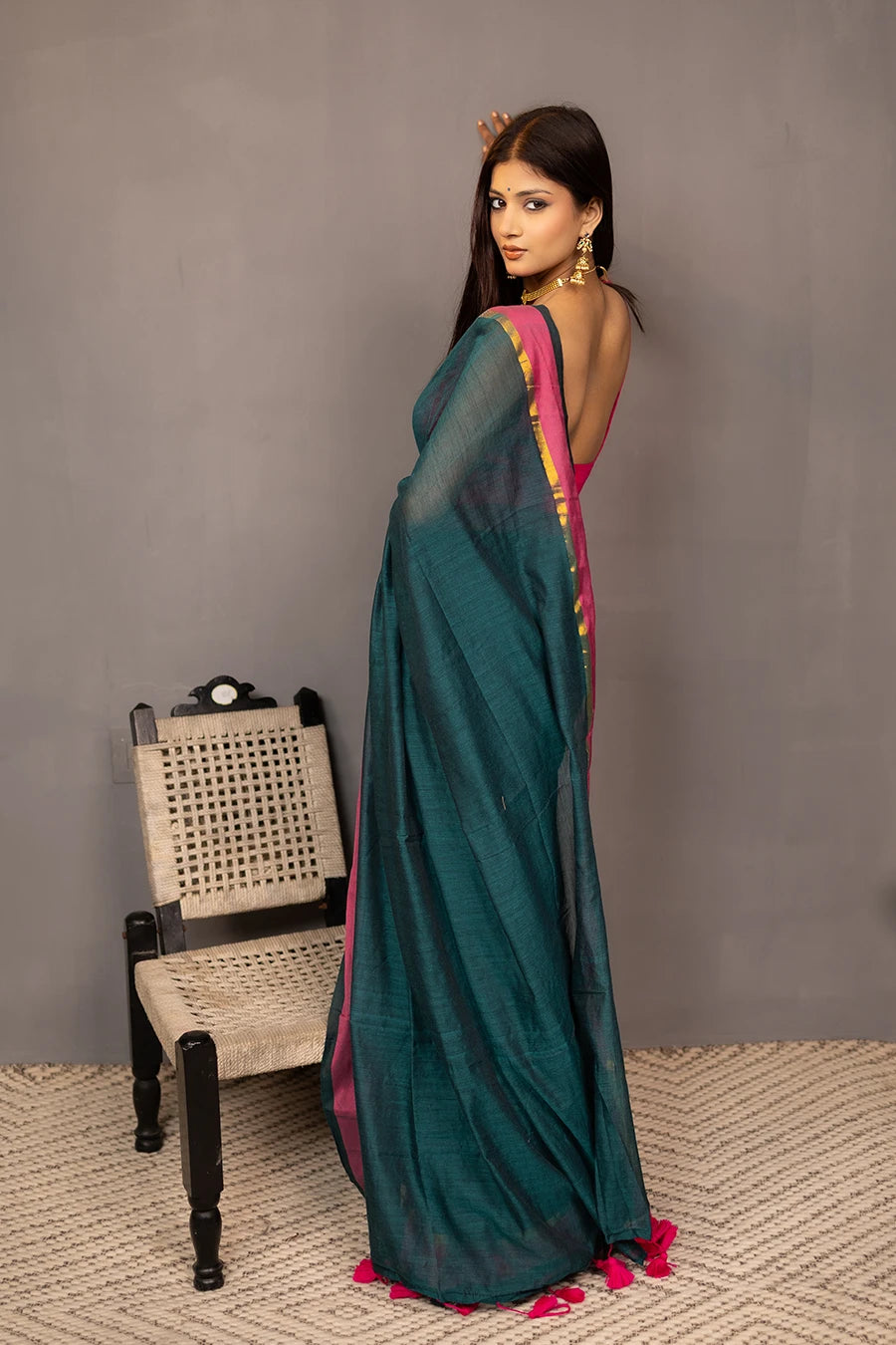 Woman holding a teal saree with pink border against a grey background