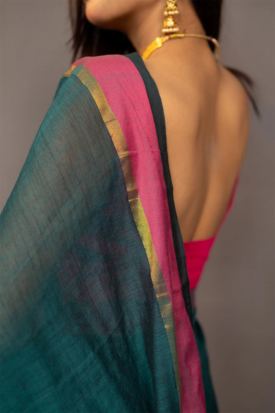 Woman holding a teal saree with pink border against a grey background