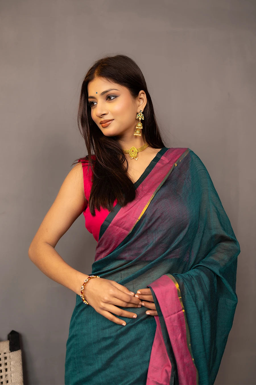 Woman holding a teal saree with pink border against a grey background