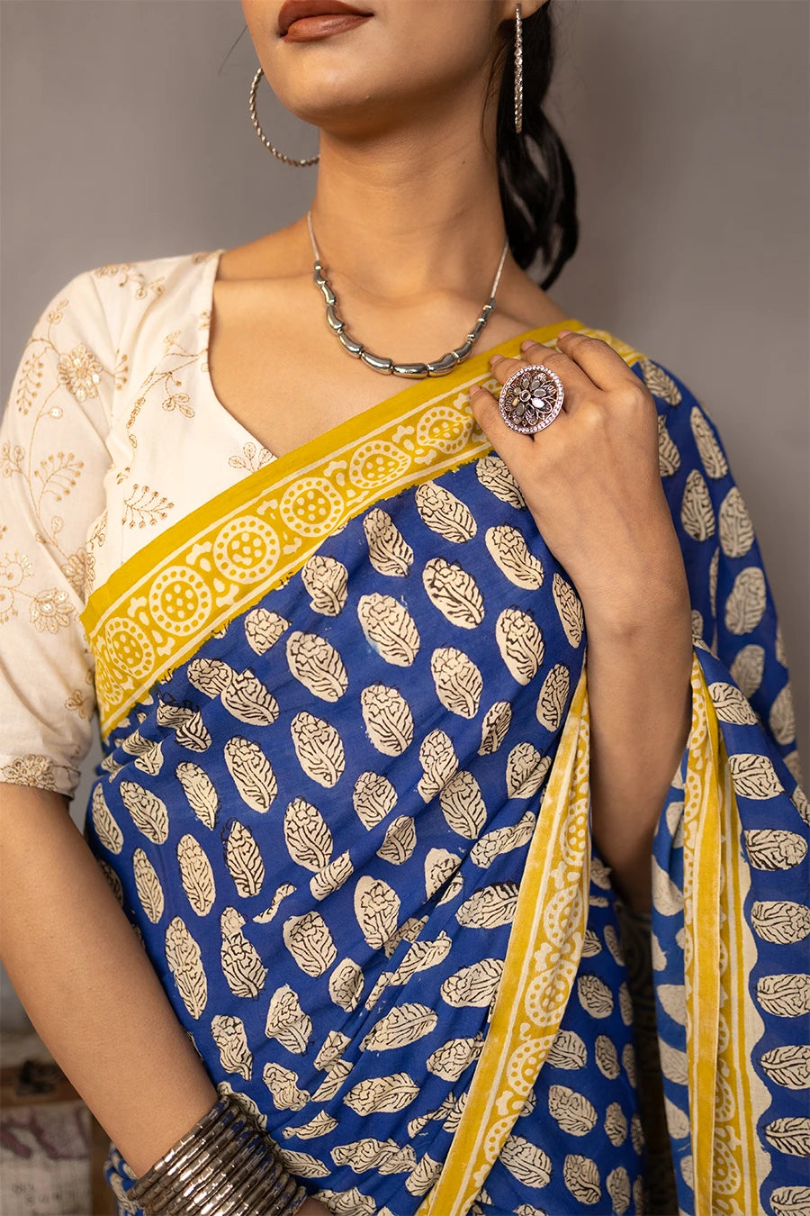 Woman wearing a blue and yellow saree standing next to vintage suitcases and books against a grey background