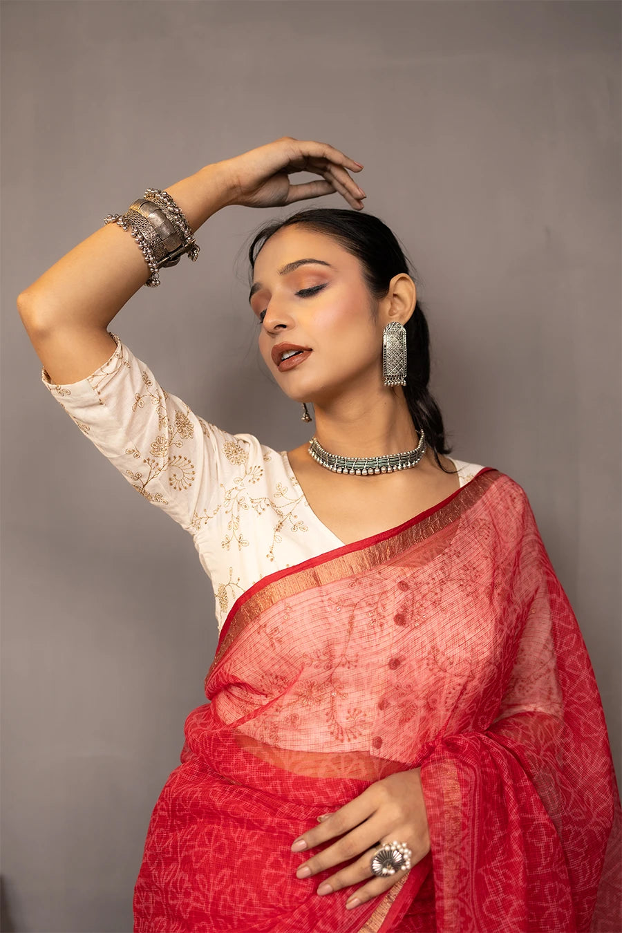 Woman wearing a red saree with a white blouse against a grey background
