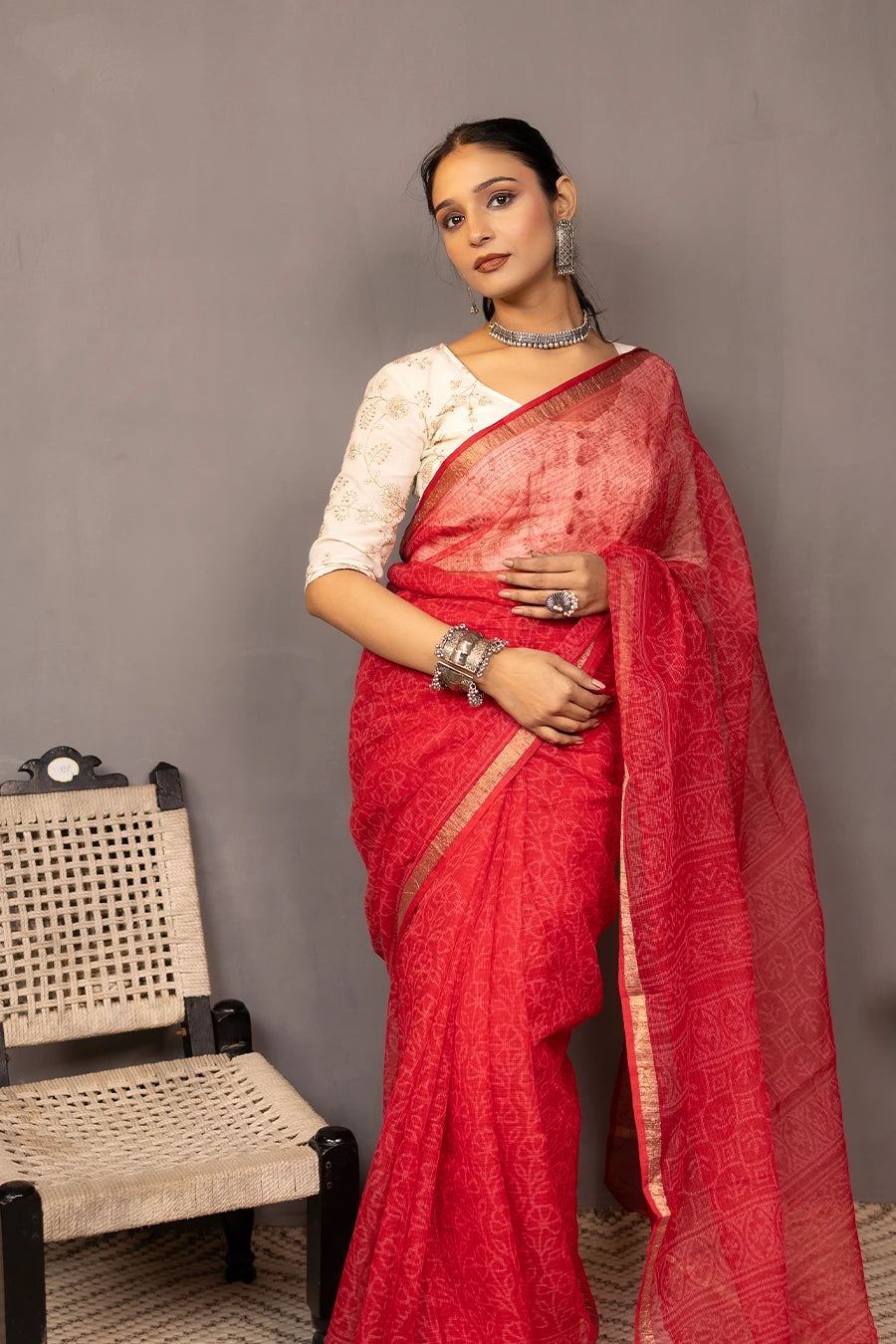 Woman wearing a red saree with a white blouse against a grey background