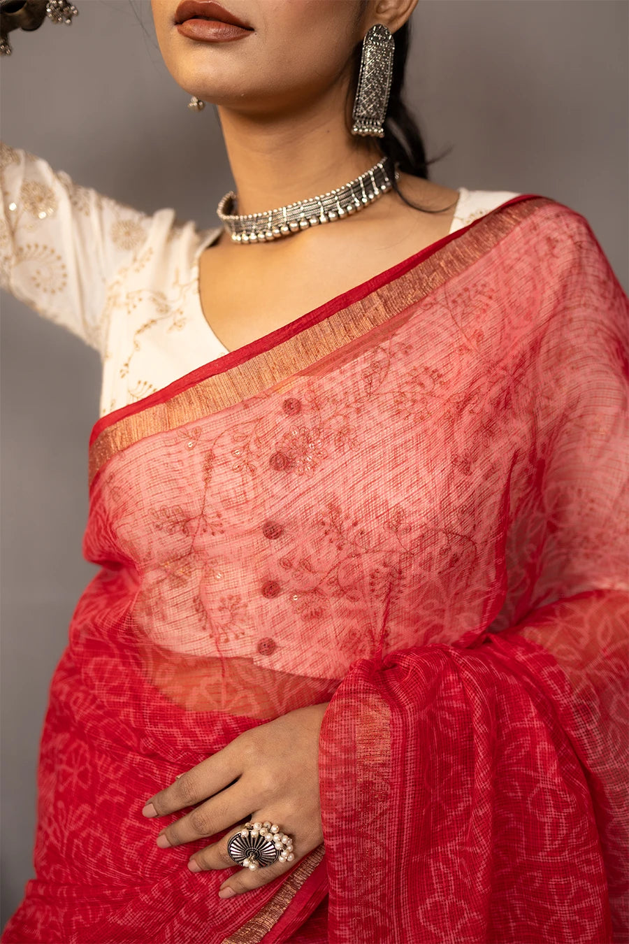 Woman wearing a red saree with a white blouse against a grey background