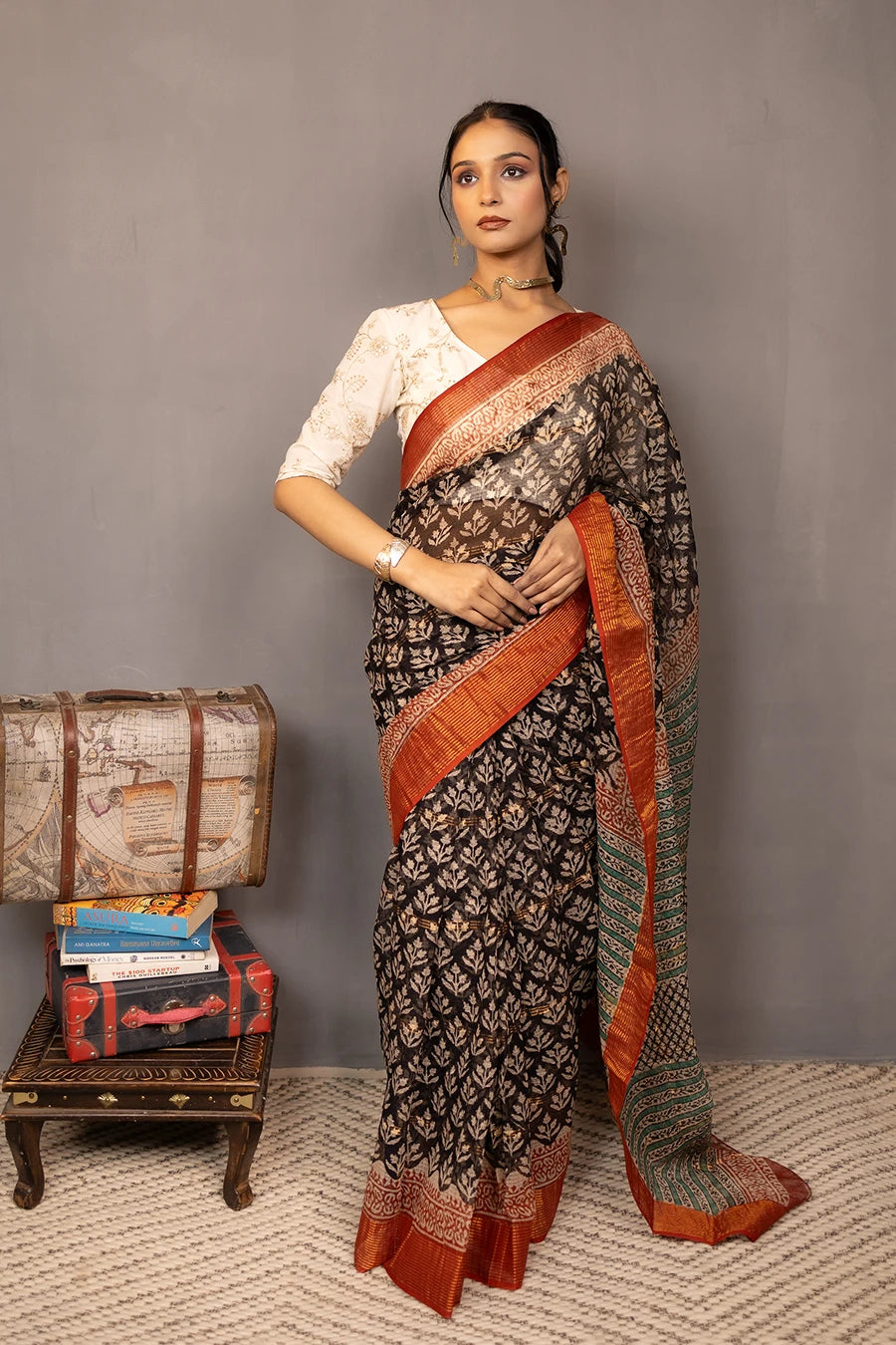 Woman wearing a traditional saree with a patterned design, standing next to vintage suitcases on a textured surface.