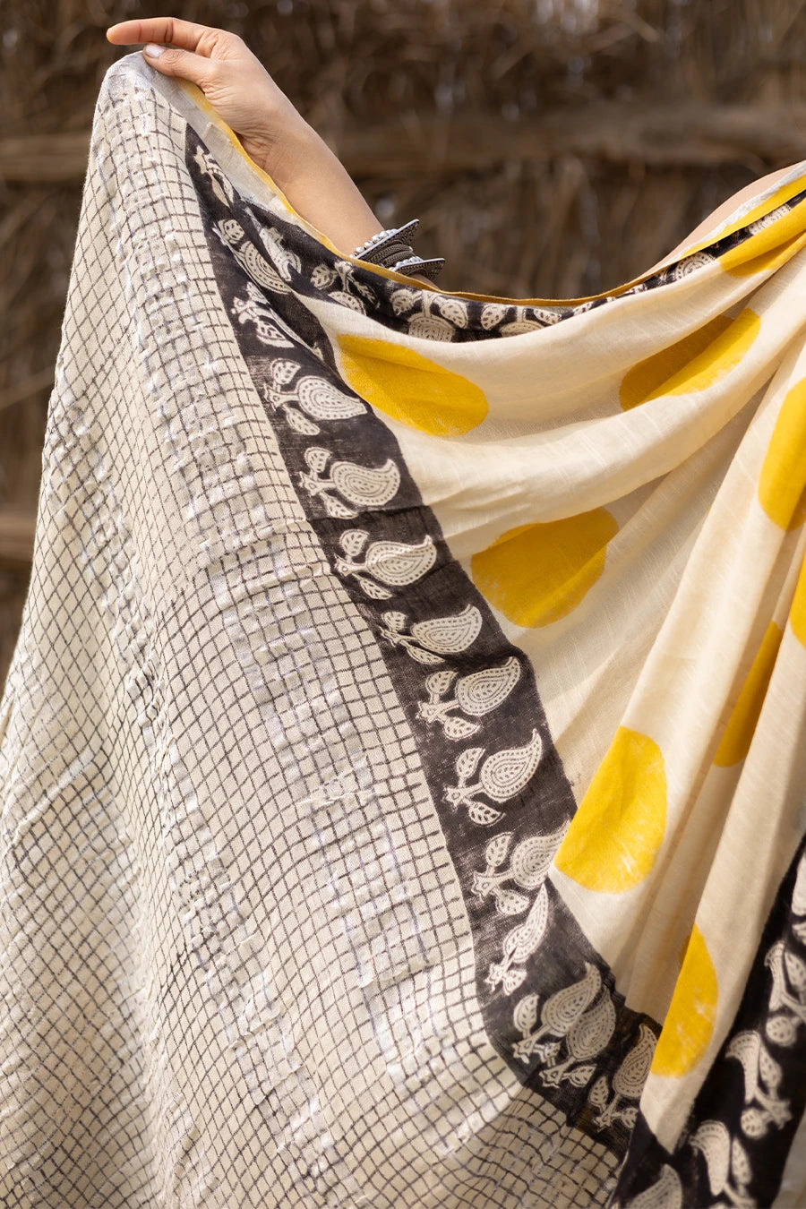 Woman wearing a traditional saree with yellow and white pattern in front of a rustic background