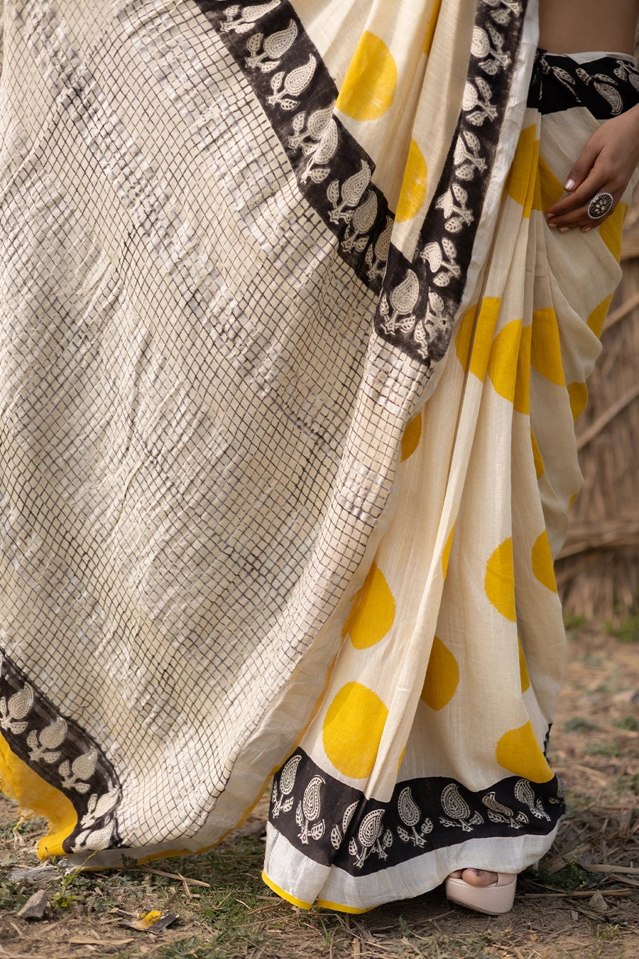 Woman wearing a traditional saree with yellow and white pattern in front of a rustic background