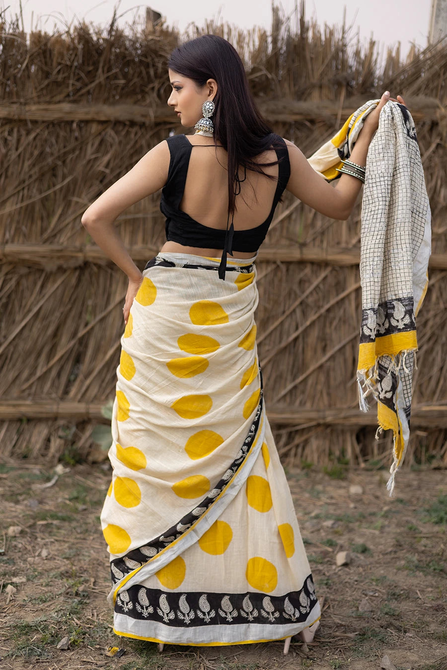 Woman wearing a traditional saree with yellow and white pattern in front of a rustic background