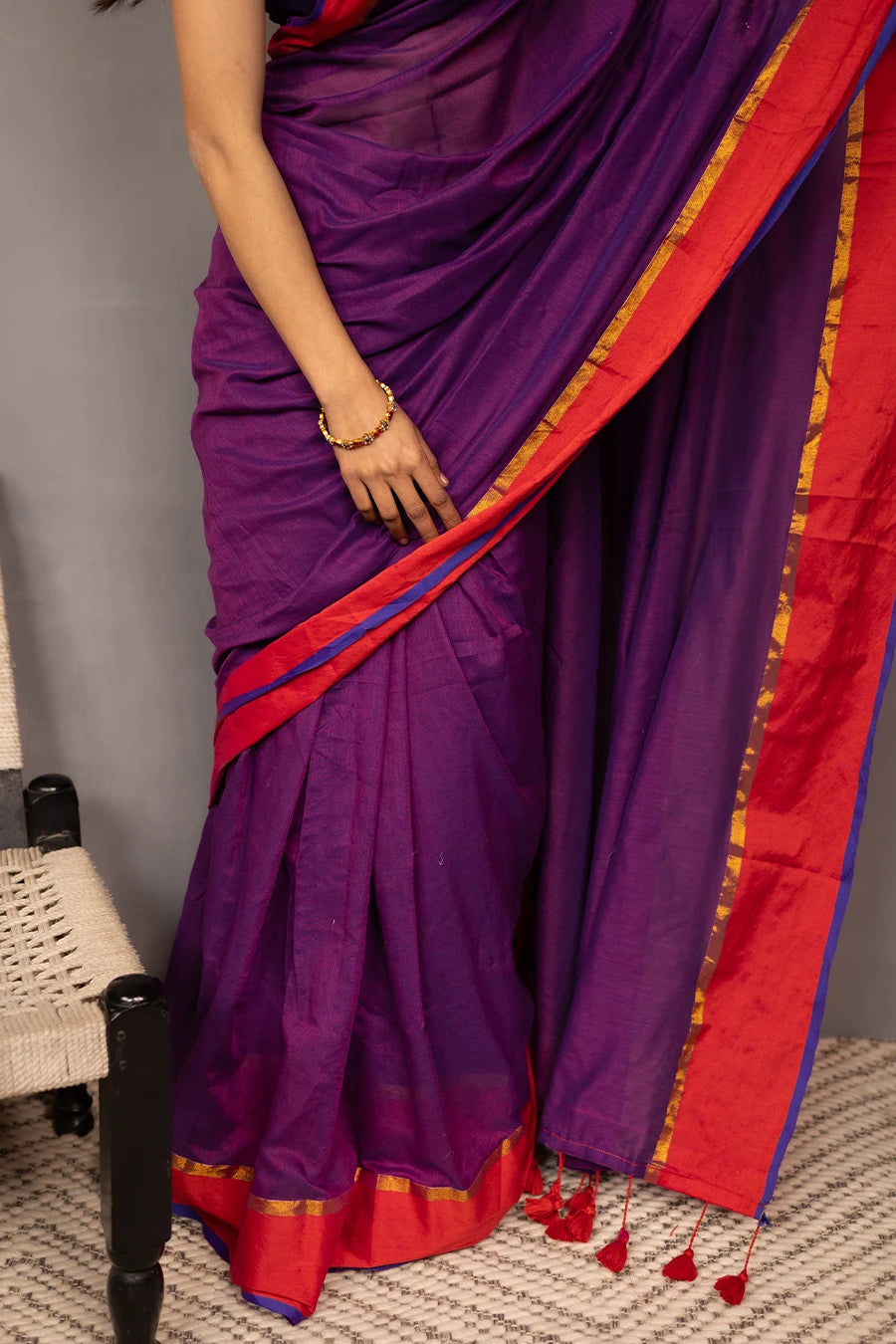 Woman wearing a purple saree with red border against a grey background
