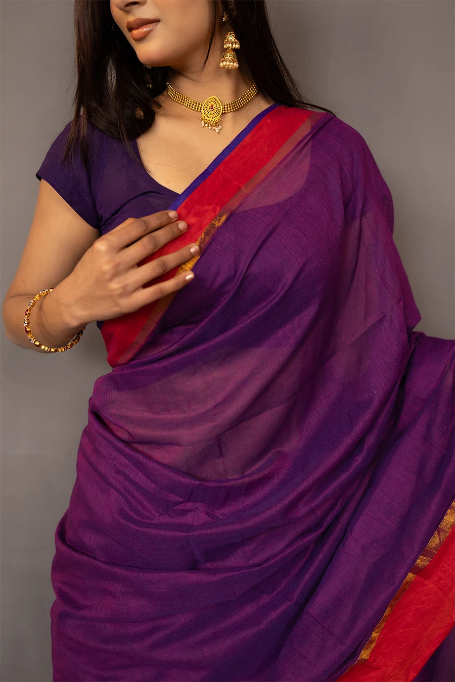 Woman wearing a purple saree with a red border against a grey background