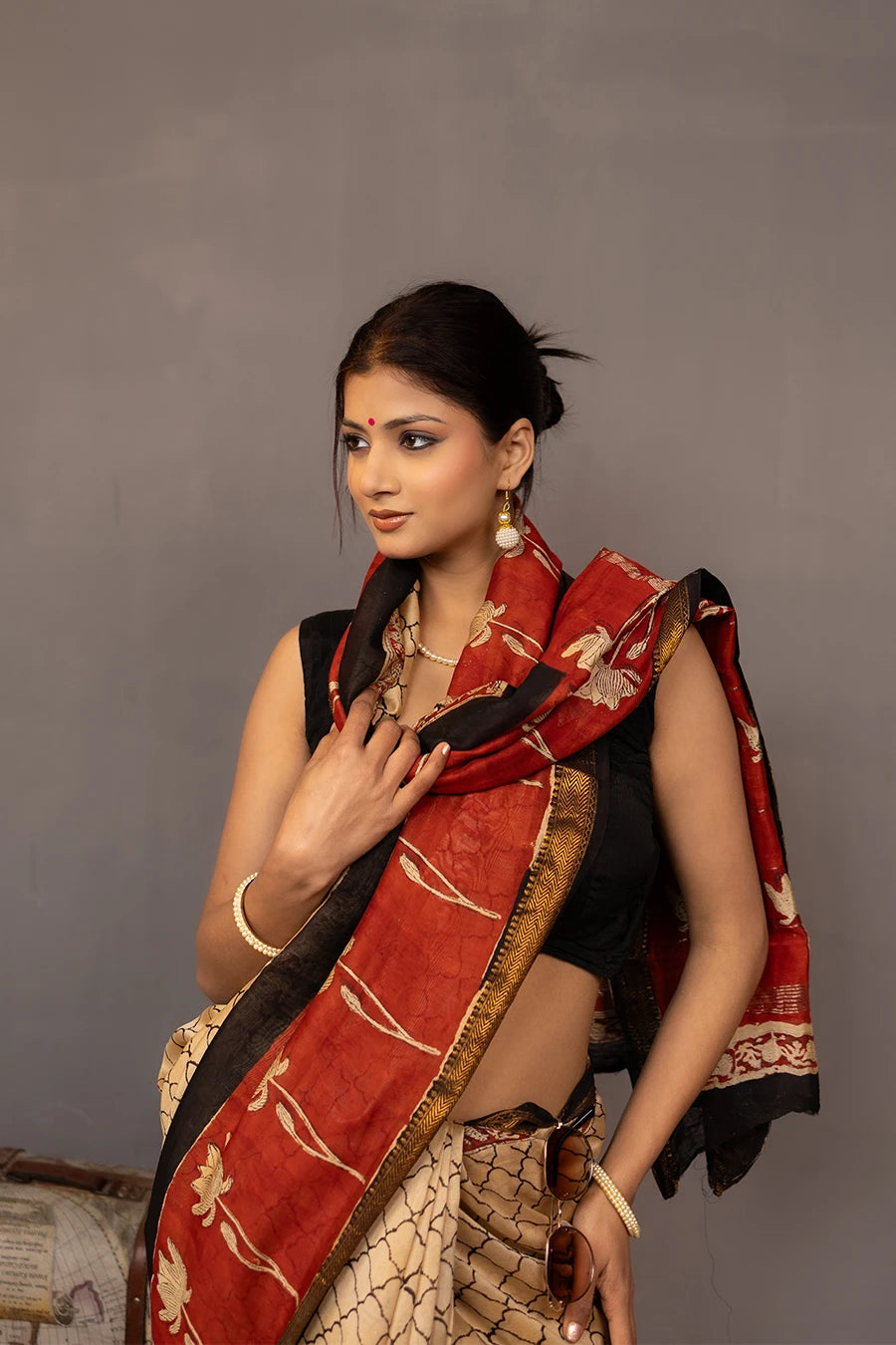 Woman wearing a traditional saree with a red border, standing next to a small table with books and a map.