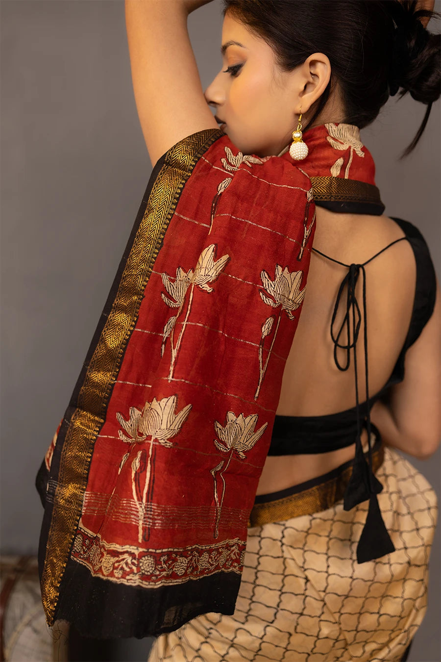 Woman wearing a traditional saree with a red border, standing next to a small table with books and a map.
