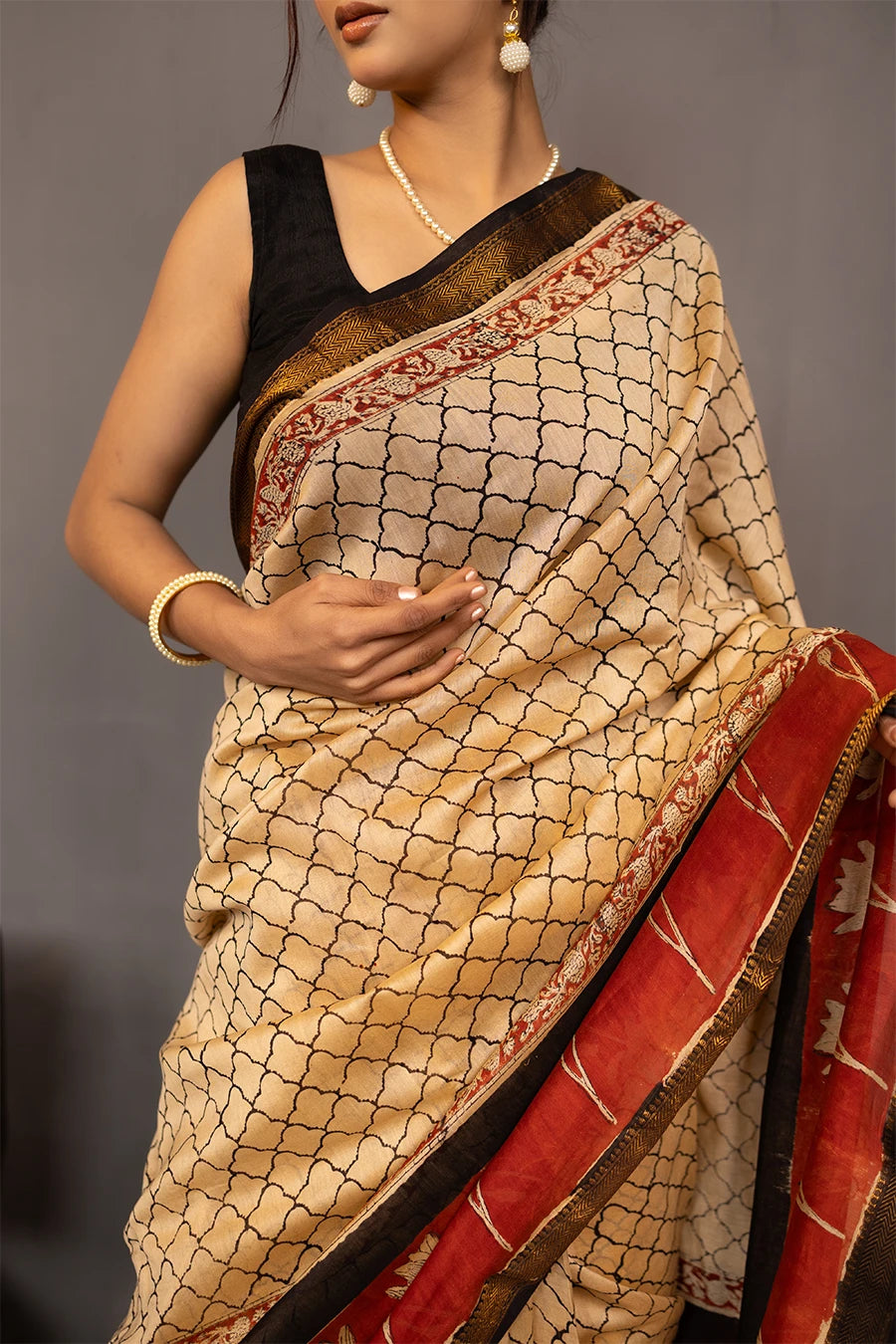Woman wearing a traditional saree with a red border, standing next to a small table with books and a map.