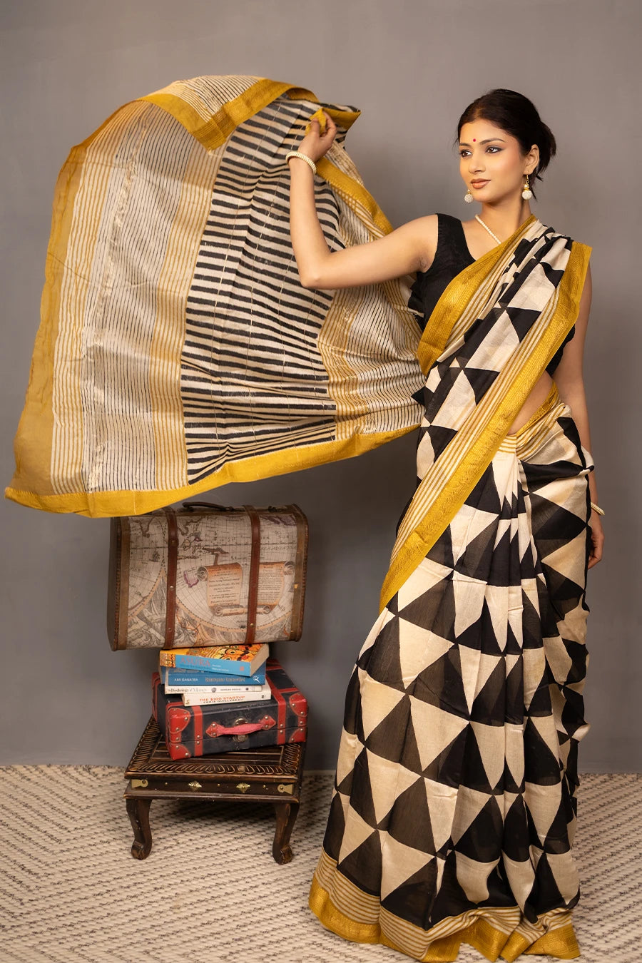 Woman wearing a black and white patterned saree with gold border, standing against a grey background.