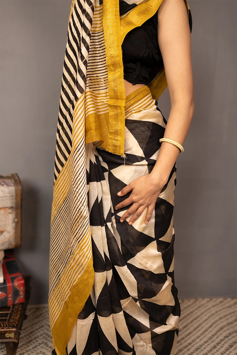 Woman wearing a black and white patterned saree with gold border, standing against a grey background.