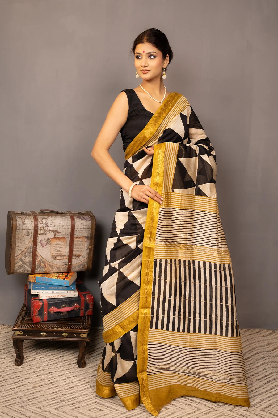 Woman wearing a black and white patterned saree with gold border, standing against a grey background.