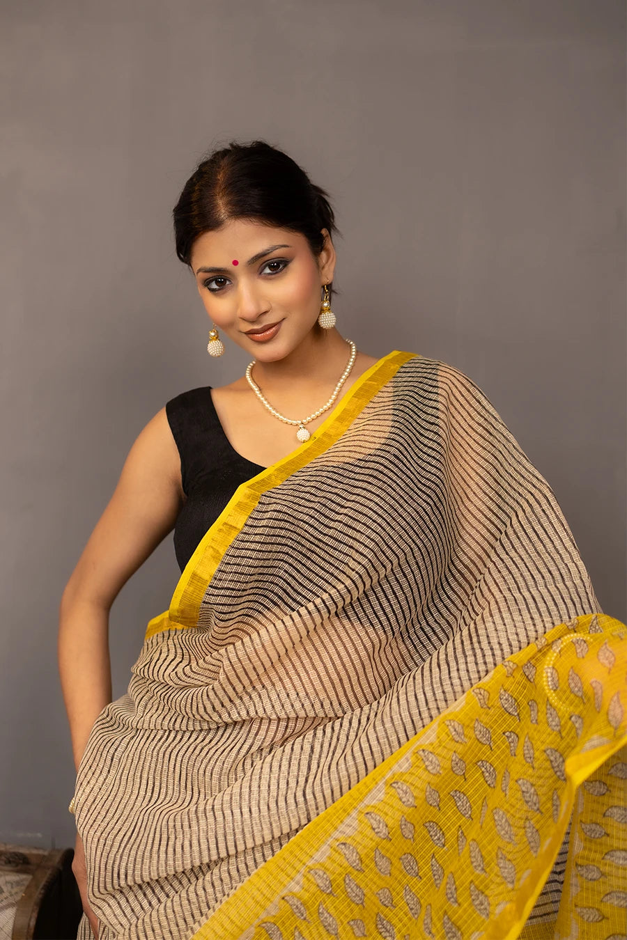 Woman wearing a beige and yellow saree with a grey background