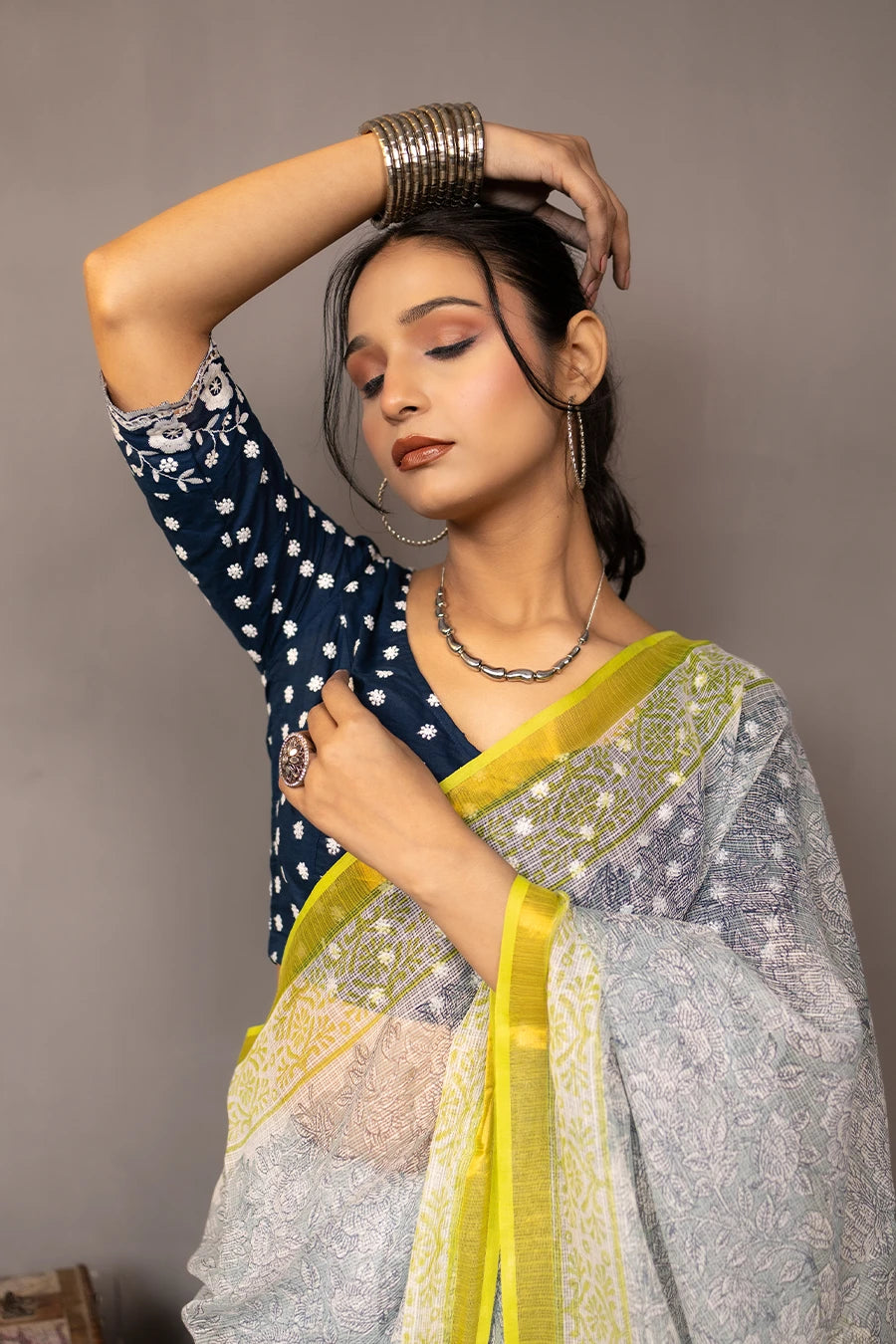 Woman in a saree standing next to a small table with books and boxes against a grey background