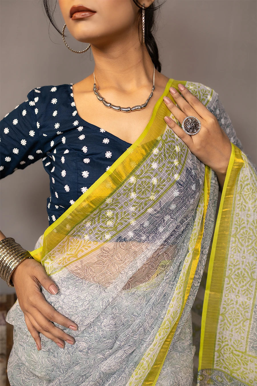 Woman in a saree standing next to a small table with books and boxes against a grey background