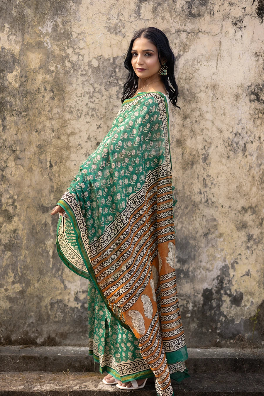 Woman in a green saree with a textured wall background