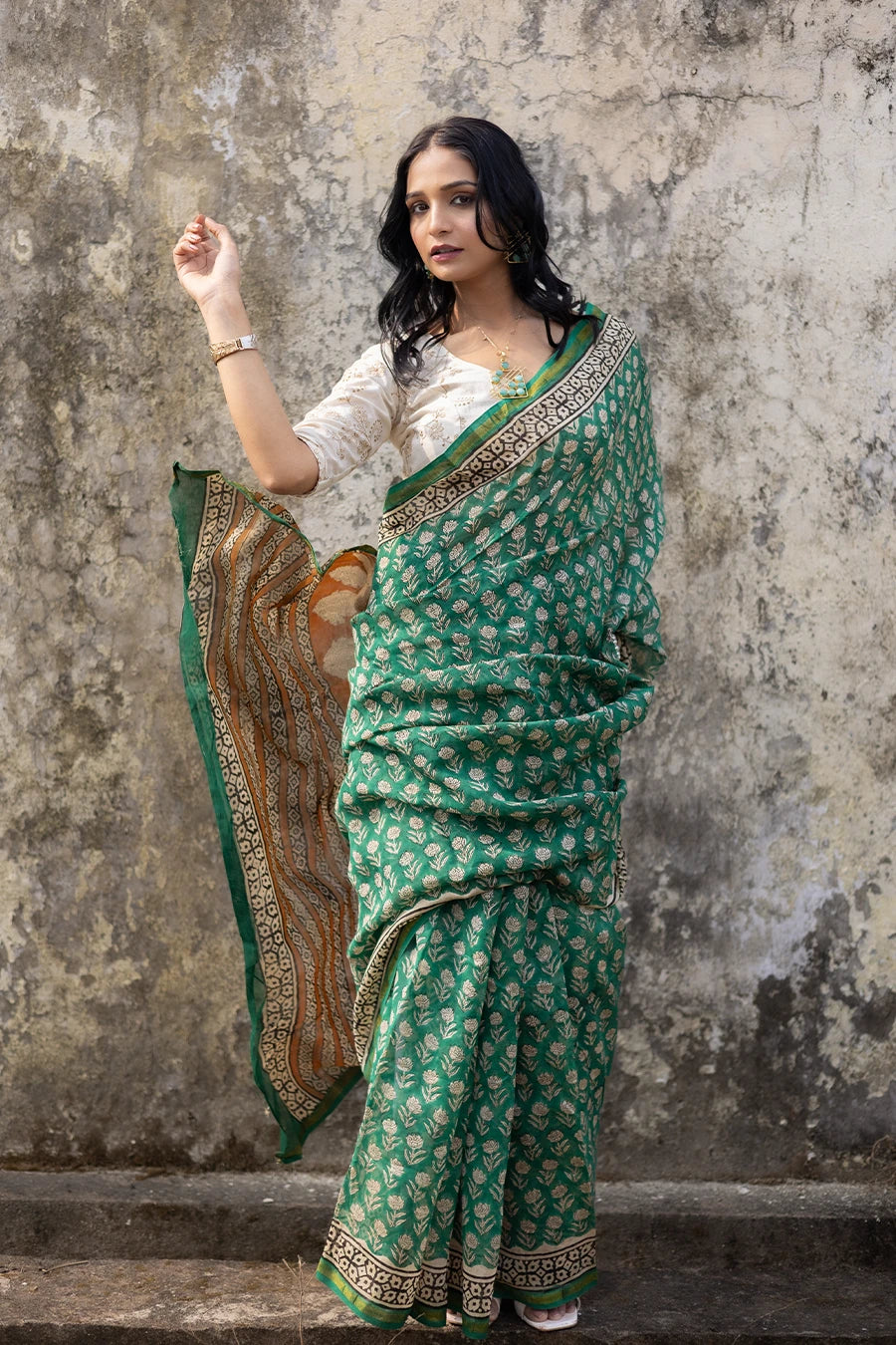 Woman in a green saree with a textured wall background